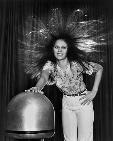 A woman's hair stands on end due to static electricity as she touches a Van de Graaf generator.